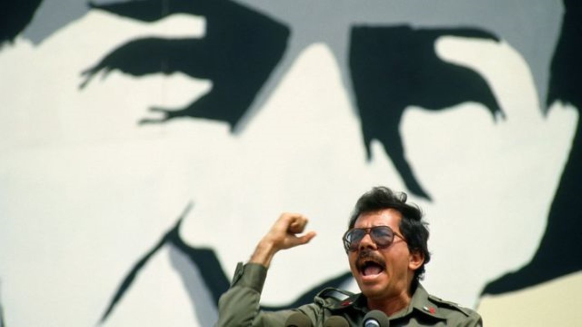 Foto histórica:  El comandante Daniel Ortega, con el puño en alto, debajo de un cuadro de Sandino