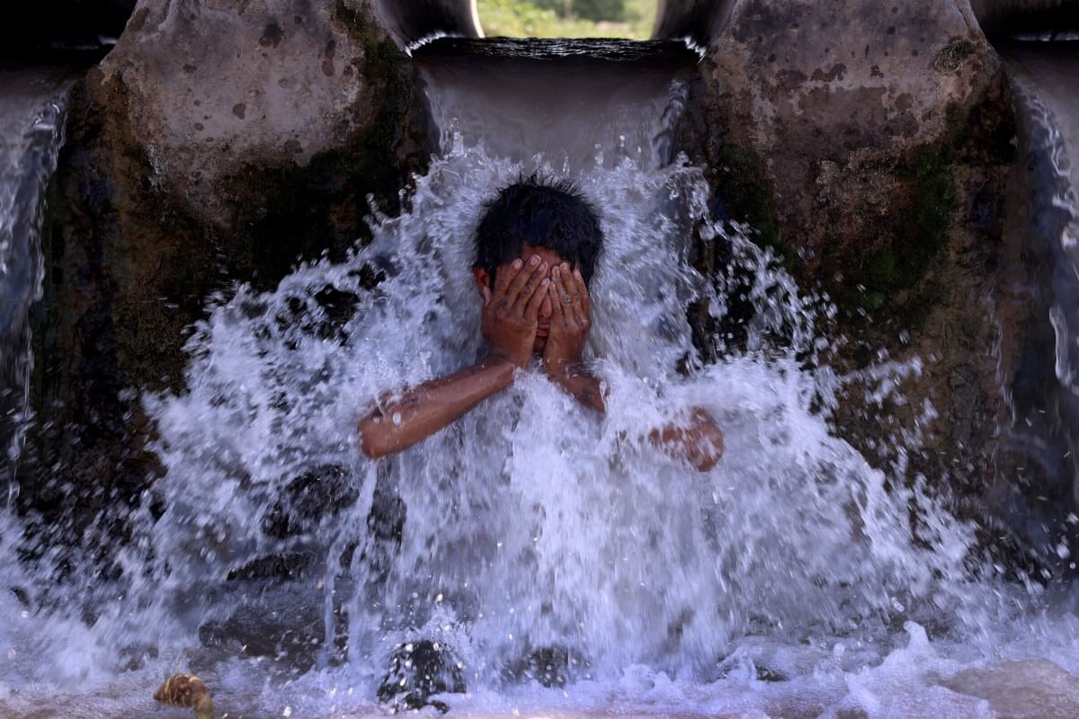 Un niño se refresca bajo una tubería de agua de un canal durante un caluroso día de verano en las afueras de Peshawar, Pakistán