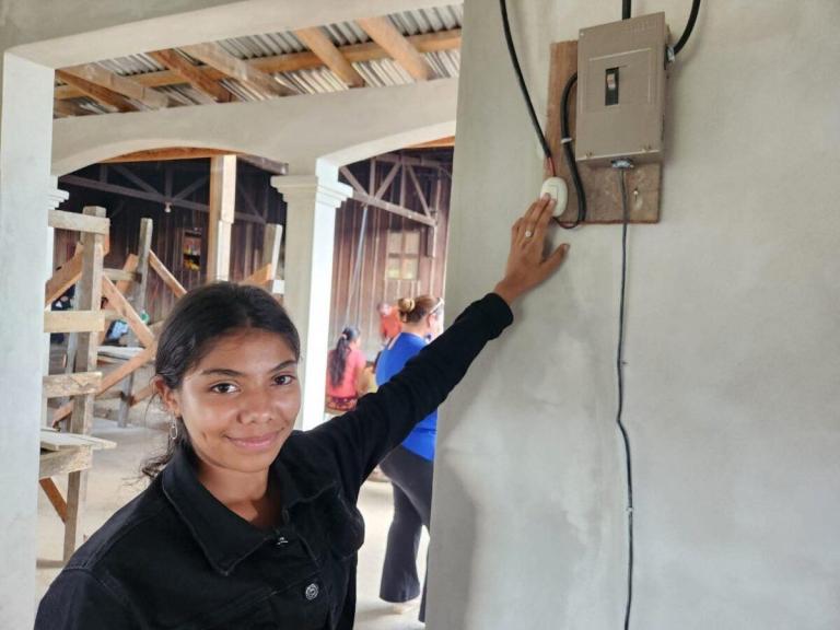 Joven sonriente enciende interruptor eléctrico en casa rural